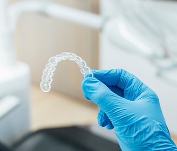 Dentist with blue gloves holding clear aligner
