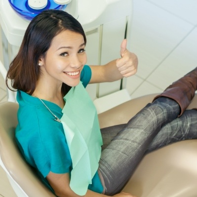 Woman giving thumbs up after preventive dentistry checkup and teeth cleaning