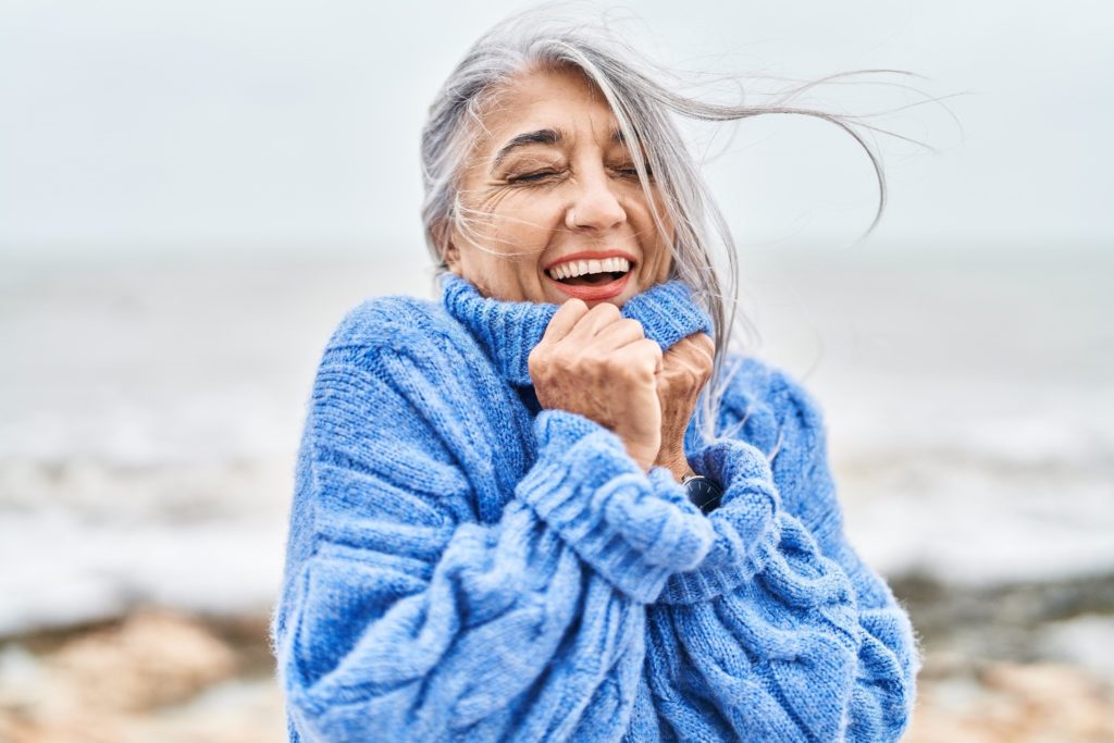 Mature woman smiling while wearing blue sweater on beach